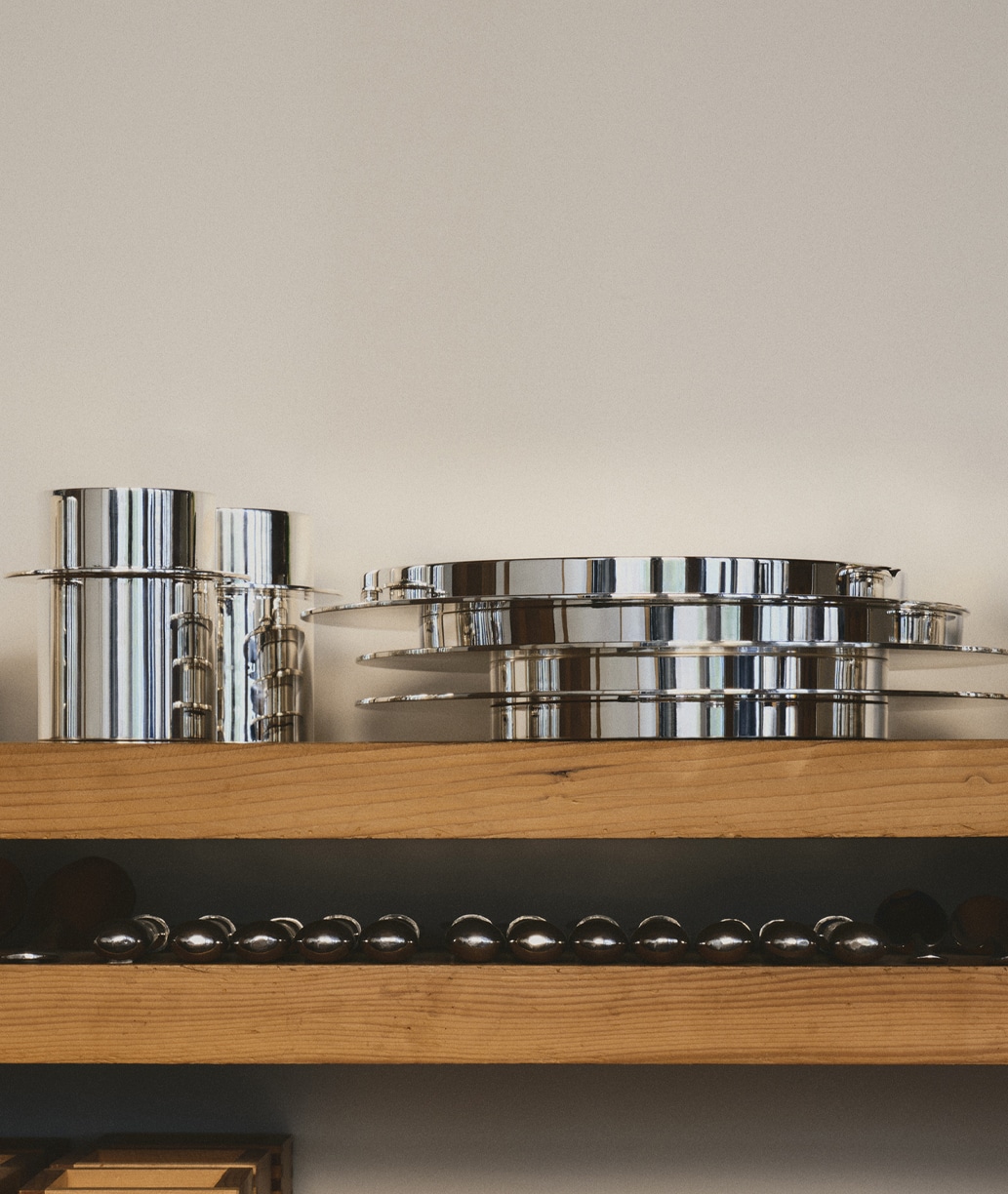 Pieces of the collection Dinner Service by Donald Judd photographed on a wood shelf with some pieces of cutlery on the down shelf