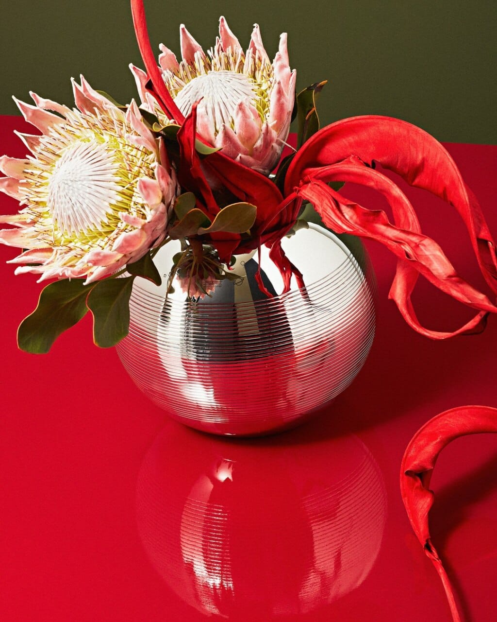Vases en métal argenté fleuri de la collection Pétanque de Puiforcat mis en scène sur une table rouge, sur un fond kaki