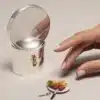 Salière de la collection Houlgate de Puiforcat en argent massif mise en scène à côté une assiette de steak et frites miniatures et une main de femme, sur un fond gris