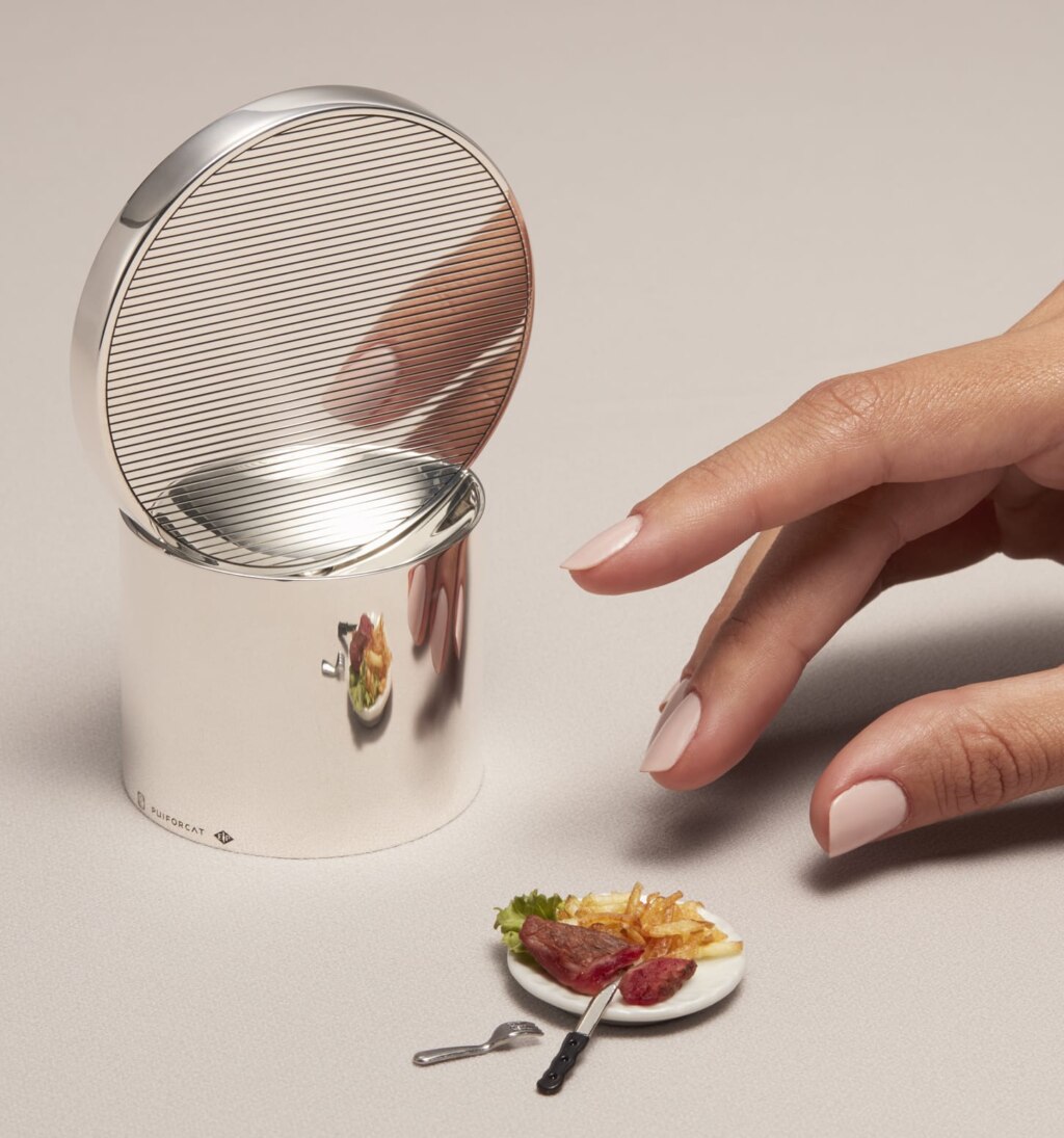 Salt mill in sterling silver from Houlgate collection from Puiforcat photographed next to a miniature version of a full plate and a woman hand