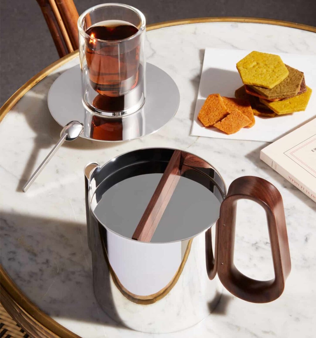 Mise en scène d'une table de café sur laquelle sont disposés une tasse à infusion, la cafetière de la collection Phi, des gâteaux et un livre