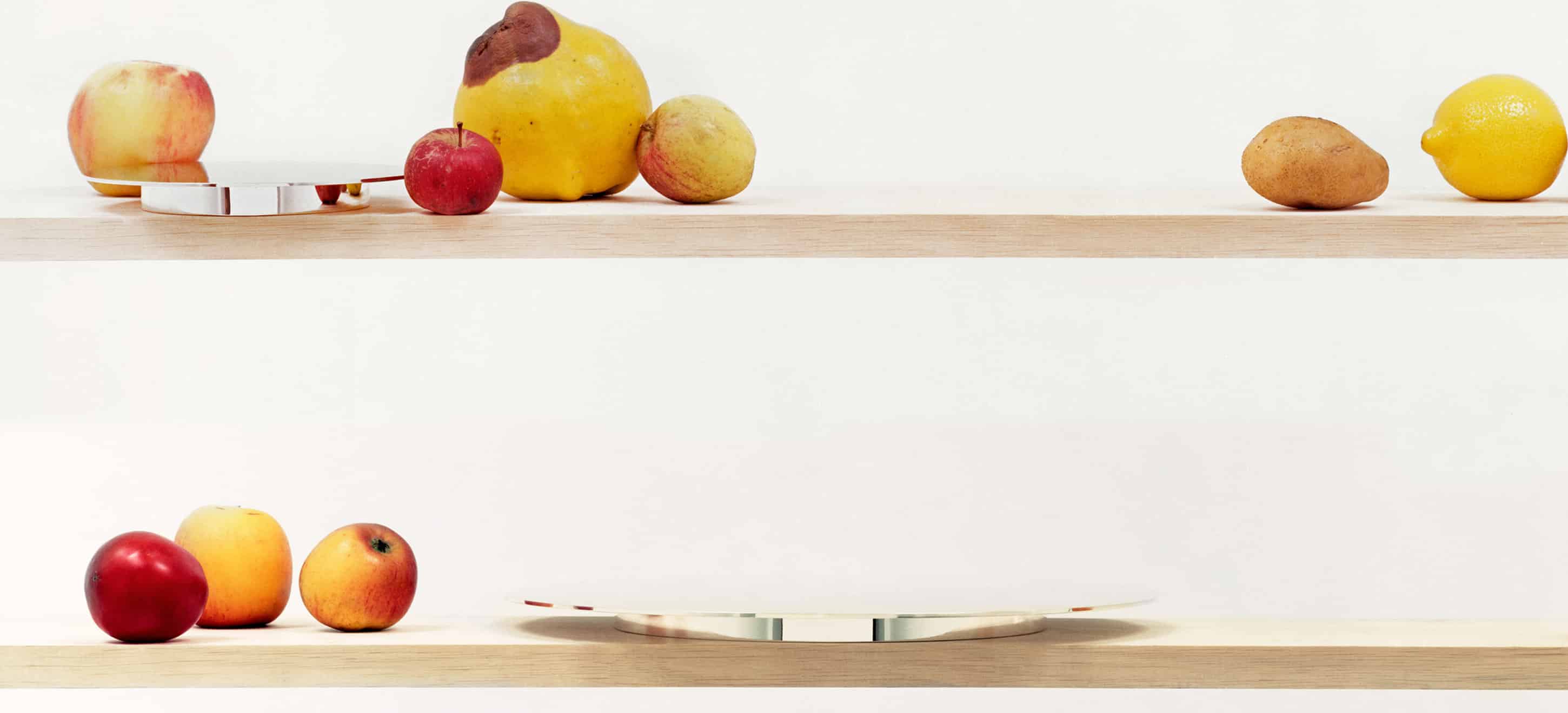 Mise en scène de pièces de la collection Dinner Service par Donald Judd de Puiforcat sur une étagère en bois, avec des légumes de toutes tailles