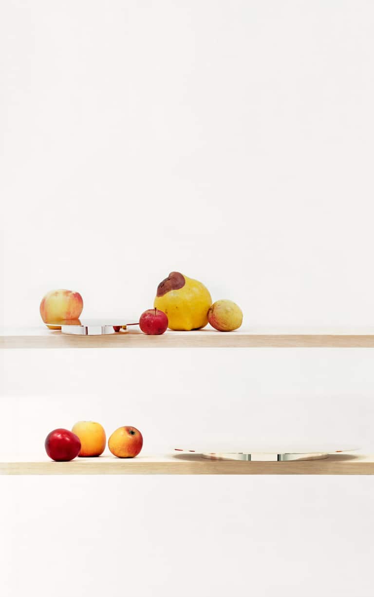 Mise en scène de pièces de la collection Dinner Service par Donald Judd de Puiforcat sur une étagère en bois, avec des légumes de toutes tailles
