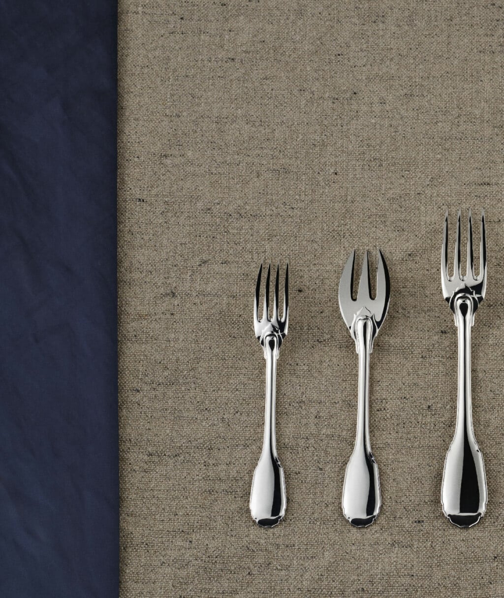 Three different forks in sterling silver from Noailles collection from Puiforcat on a grey table cloth