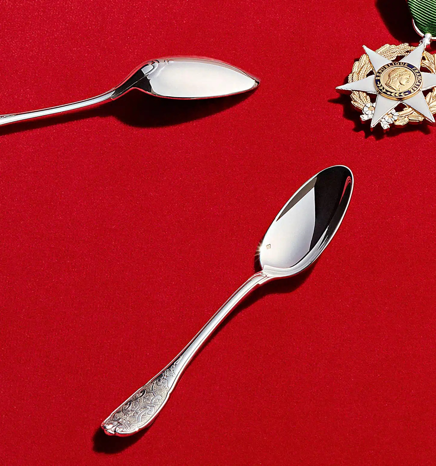 Couverts de table de la collection Elysée en argent massif et jade photographiés sur un fond rouge à côté d'une médaille en symbole de la république française