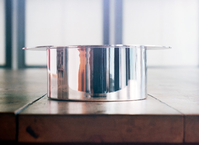 Salad bowl in sterling silver from Dinner Service by Donald Judd on a wood table in a very bright room