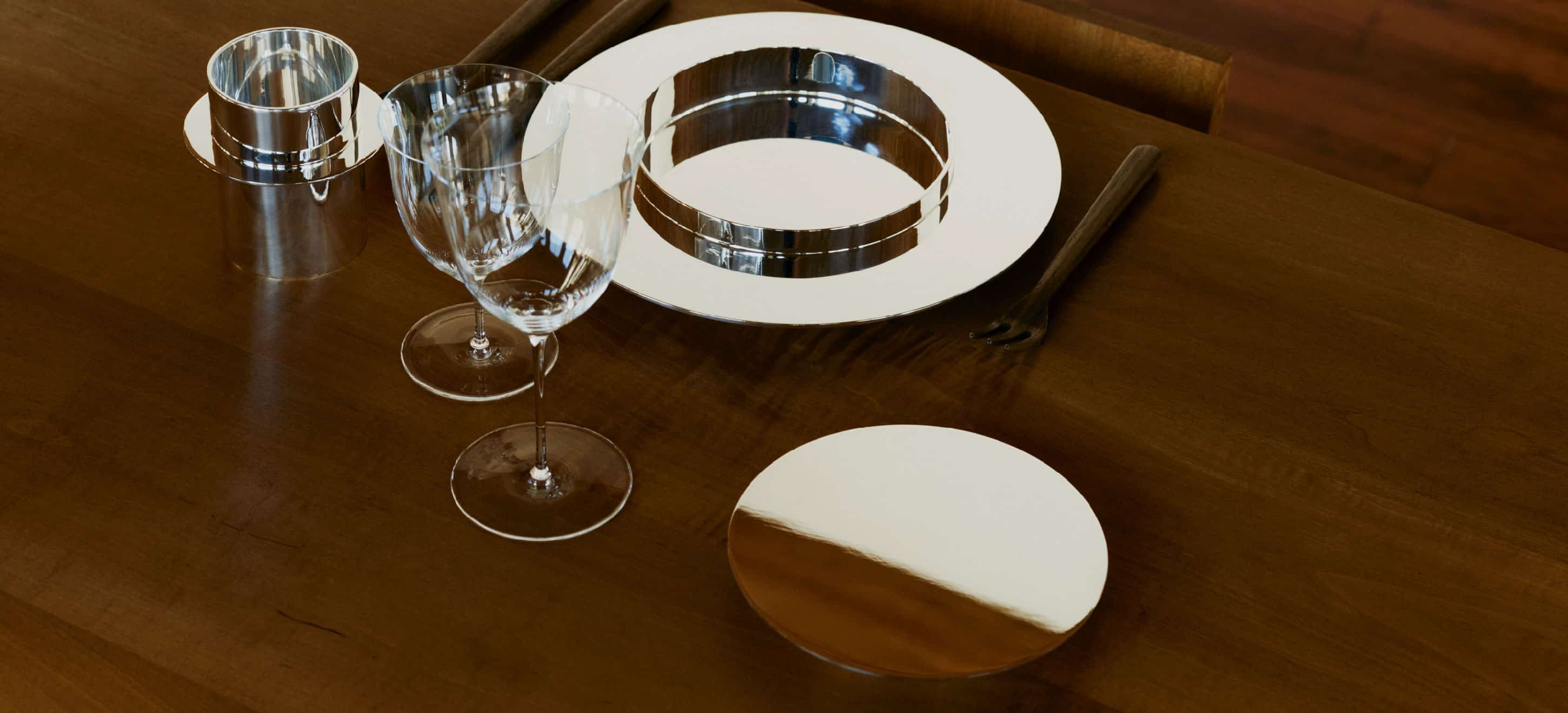 Une assiette à dessert, une gobelet et une assiette à pain de la collection Dinner Service par Donald Judd mis en scène sur une table en bois avec des verres en verre et des couverts en bois