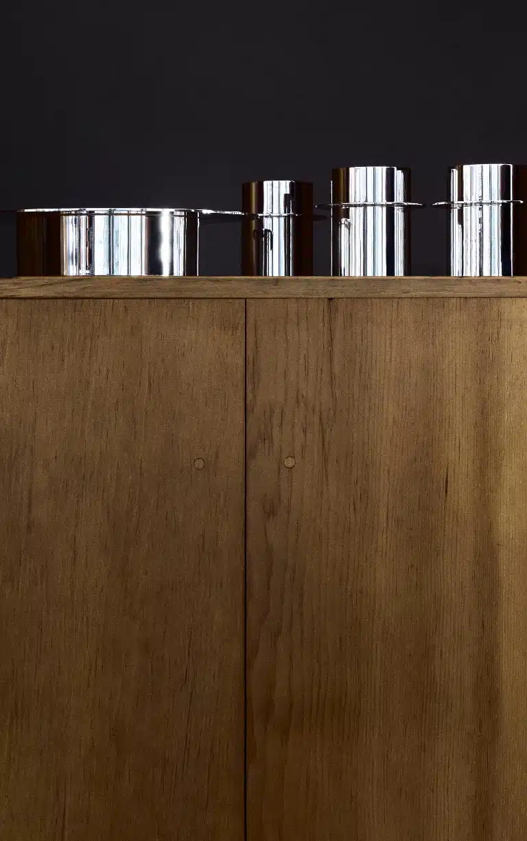 Un saladier et trois gobelets de la collection Dinner Service par Donald Judd mis en scène sur une étagère en bois et sur fond bleu marine