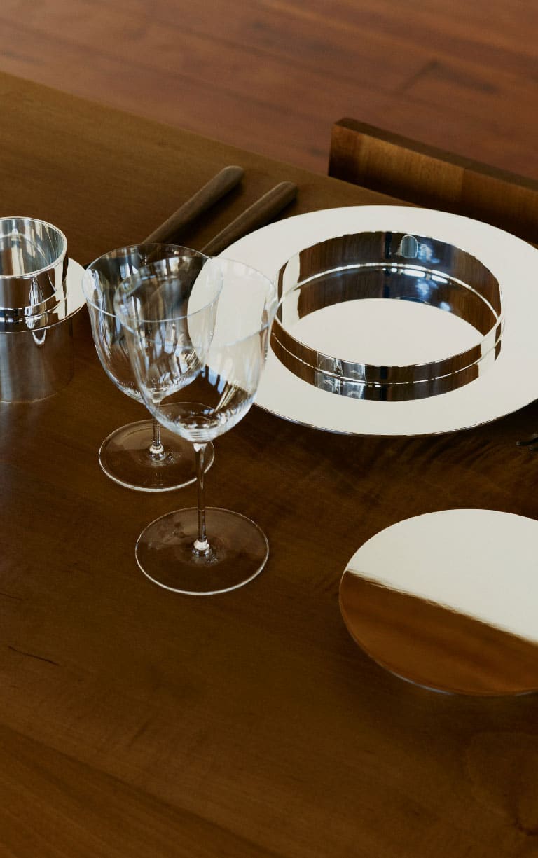Une assiette à dessert, une gobelet et une assiette à pain de la collection Dinner Service par Donald Judd mis en scène sur une table en bois avec des verres en verre et des couverts en bois