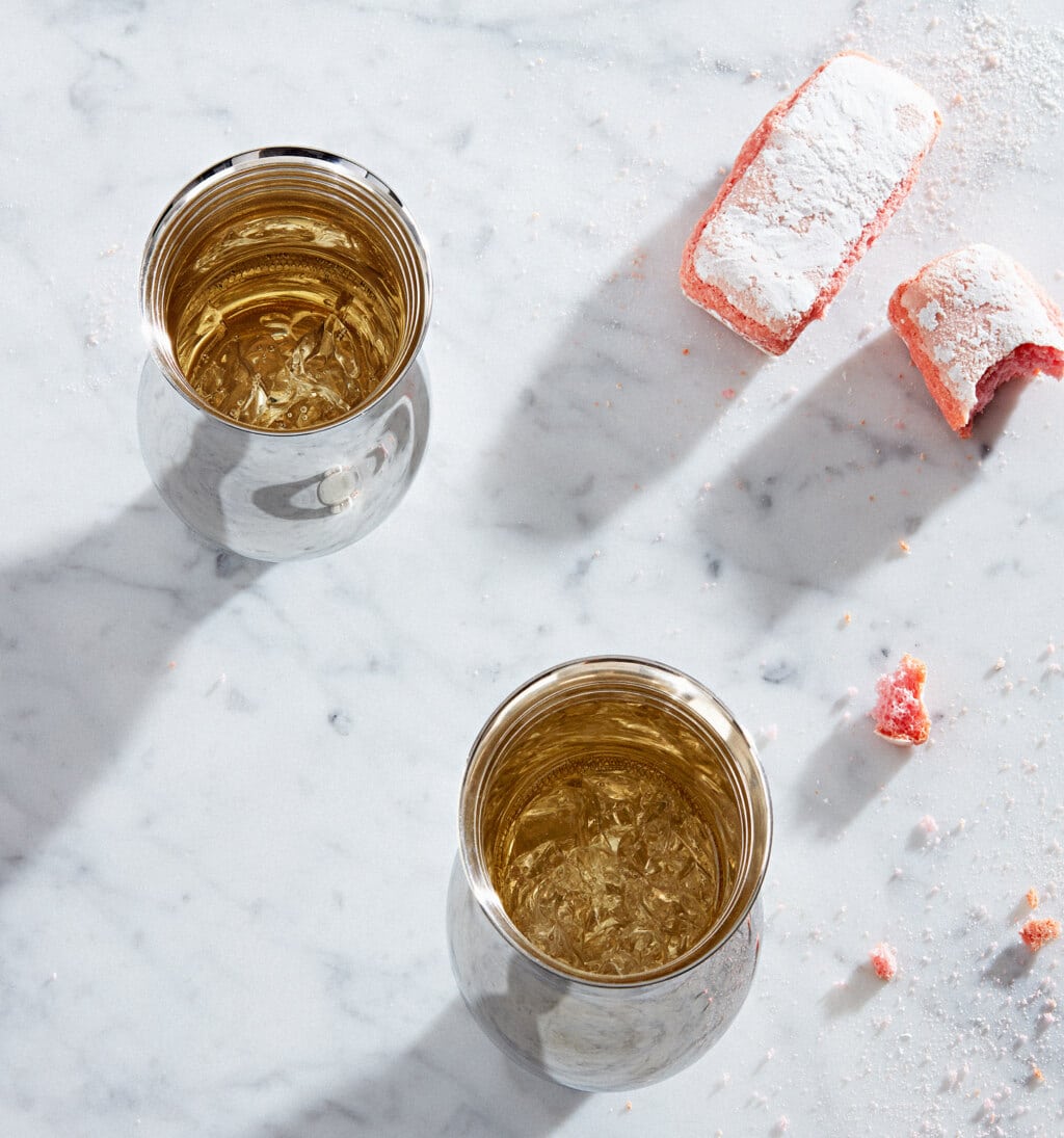 Two tumblers in sterling silver from Pour le Champagne collection, on a white marble table, photographed with pastries