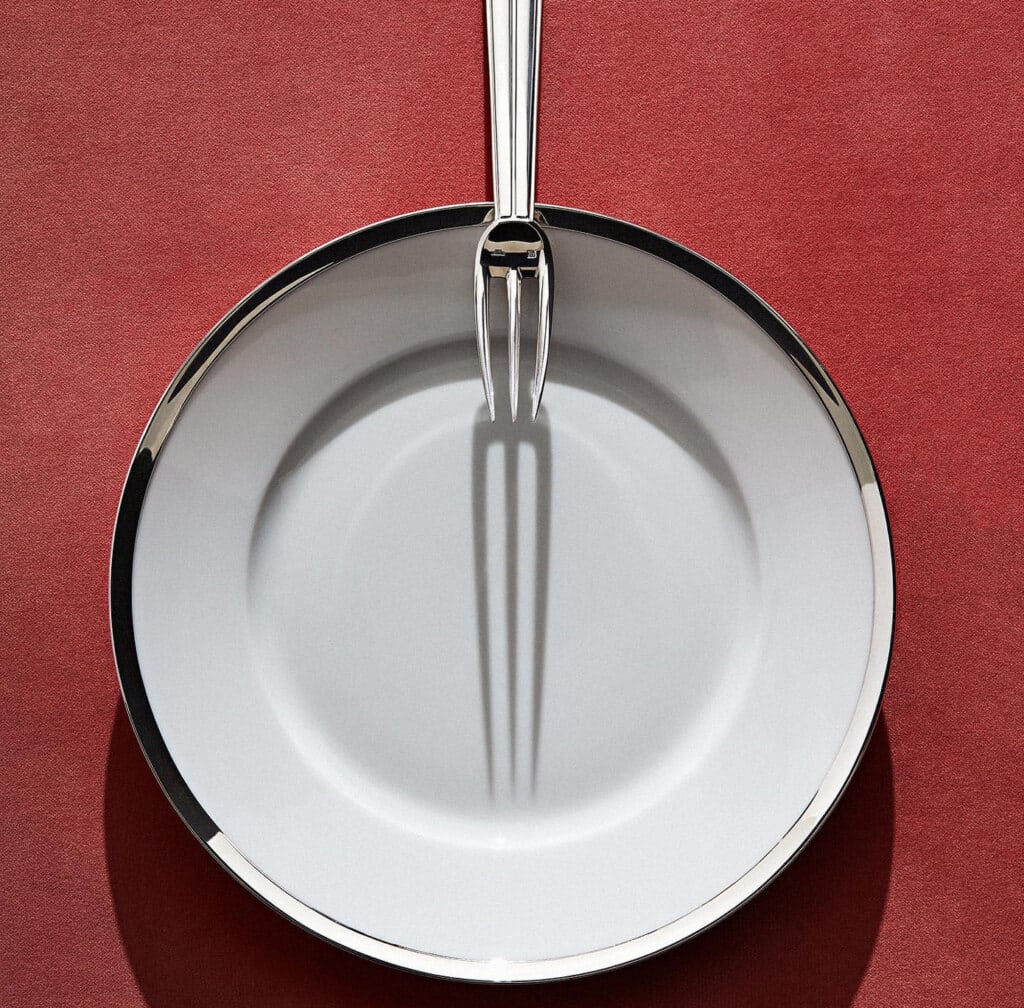 Puiforcat Cercle d'orfèvre collection in porcelain and sterling silver photographed with a Chantaco table fork on a red background