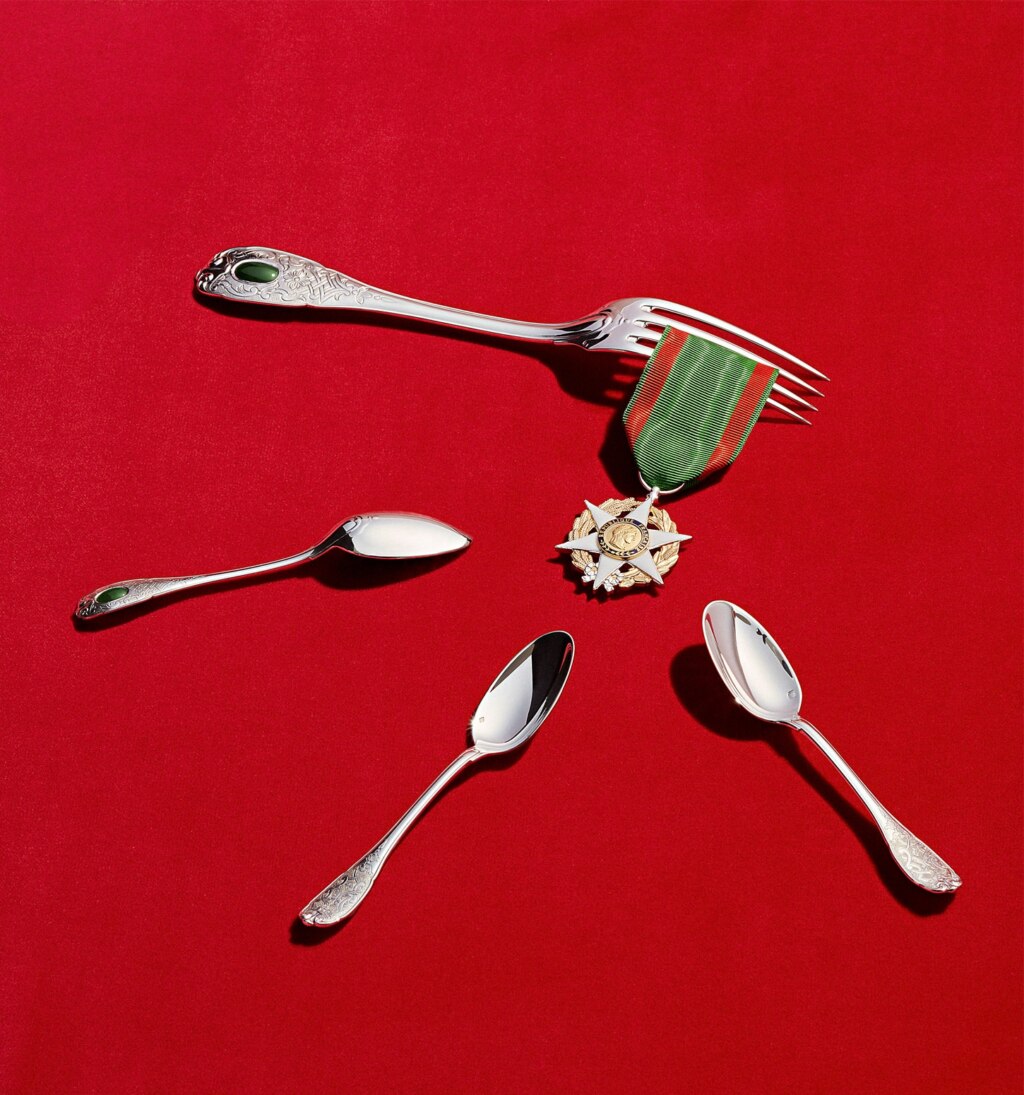 Couverts de table de la collection Elysée en argent massif et jade photographiés sur un fond rouge à côté d'une médaille en symbole de la république française