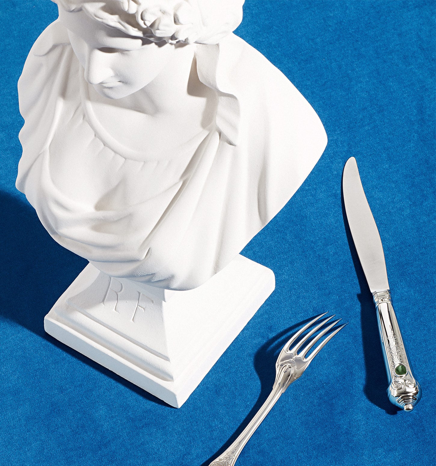 Fourchette et couteau de table de la collection Elysée photographiés sur un fond bleu à côté d'un buste de Marianne en symbole de la république française