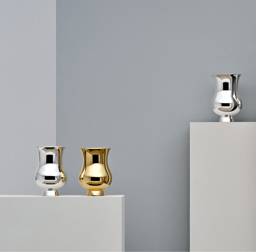Three tumblers in sterling silver from Pour le Champagne collection from Puiforcat photographed on steles of different heights in front of a grey wall