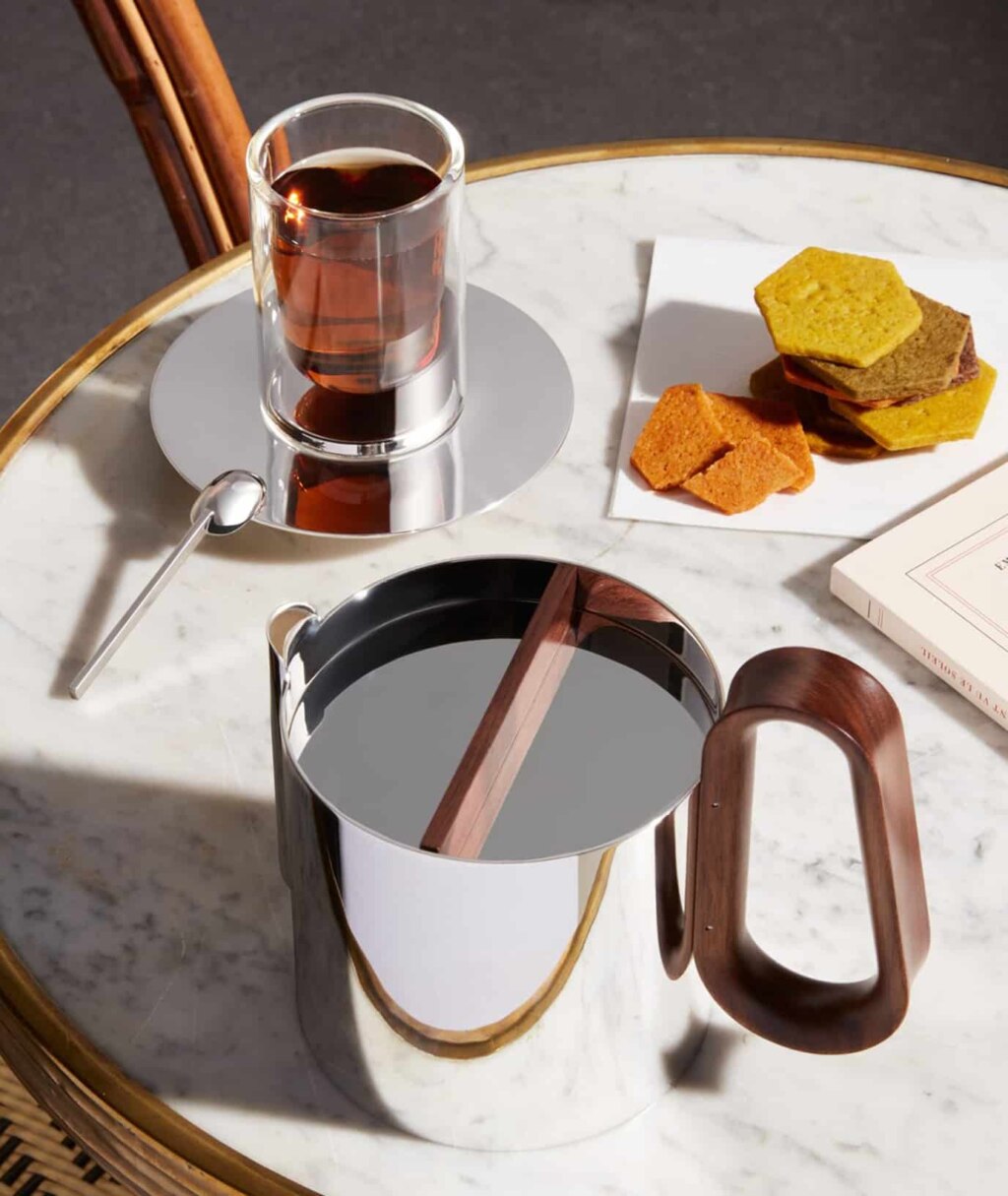 Mise en scène d'une table de café sur laquelle sont disposés une tasse à infusion, la cafetière de la collection Phi, des gâteaux et un livre