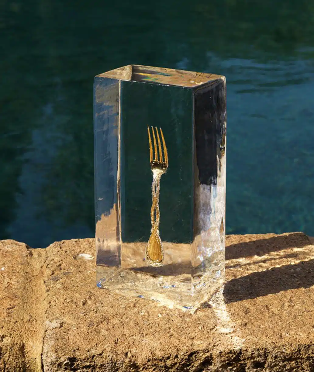 Table fork in sterling silver and gold gilt finish from Royal collection Royal from Puiforcat photographed in an ice cube, fixed upon a stone in front of a river