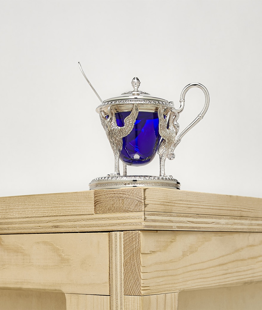 Biennais mustard pot photographed on a wood case on a grey background