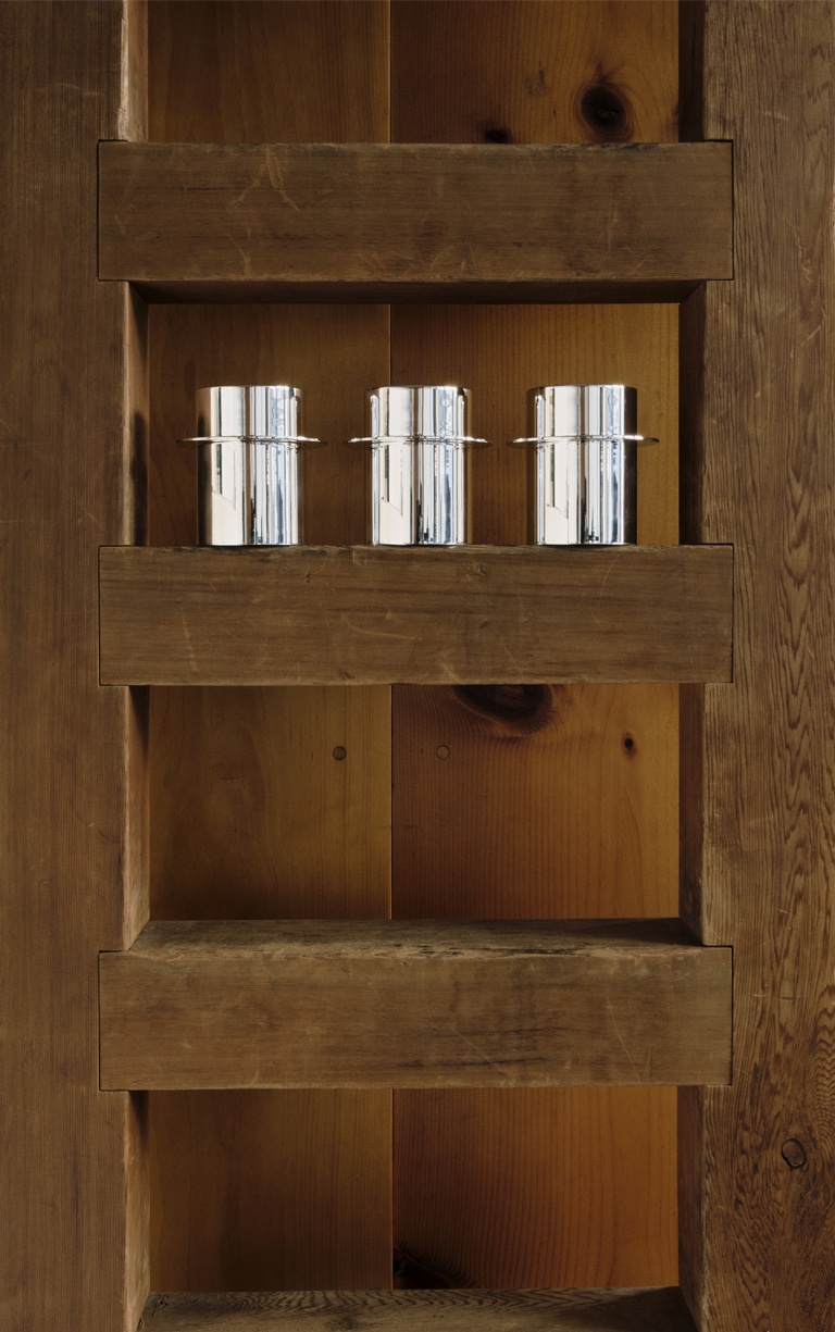 Trois gobelets de la collection Dinner Service par Donald Judd posés sur une étagère en bois