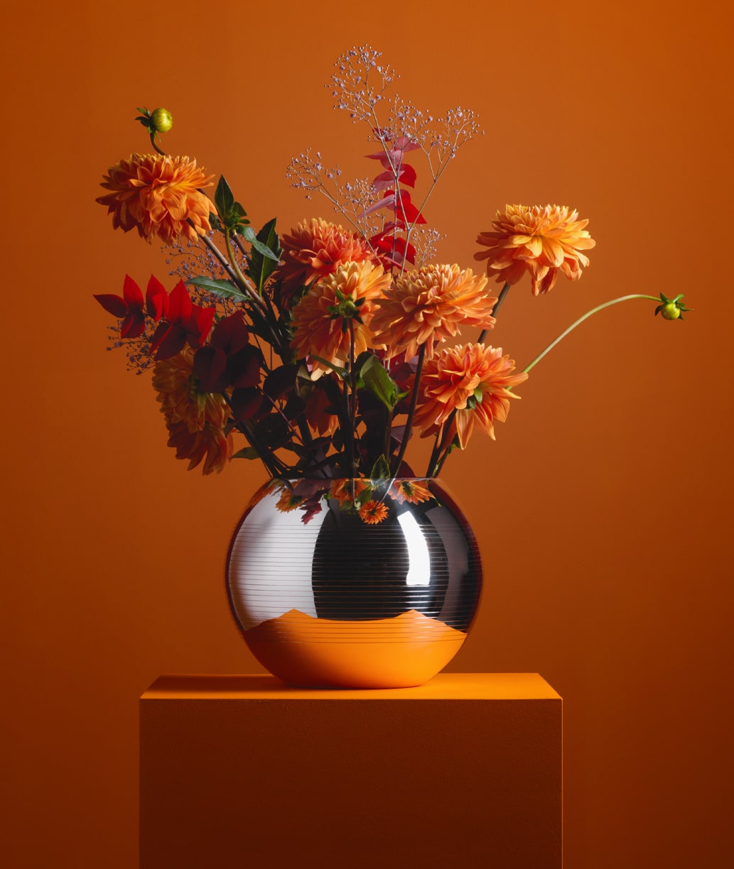 Vases en métal argenté fleuri de la collection Pétanque de Puiforcat mis en scène sur une stèle orange, sur un fond orangé