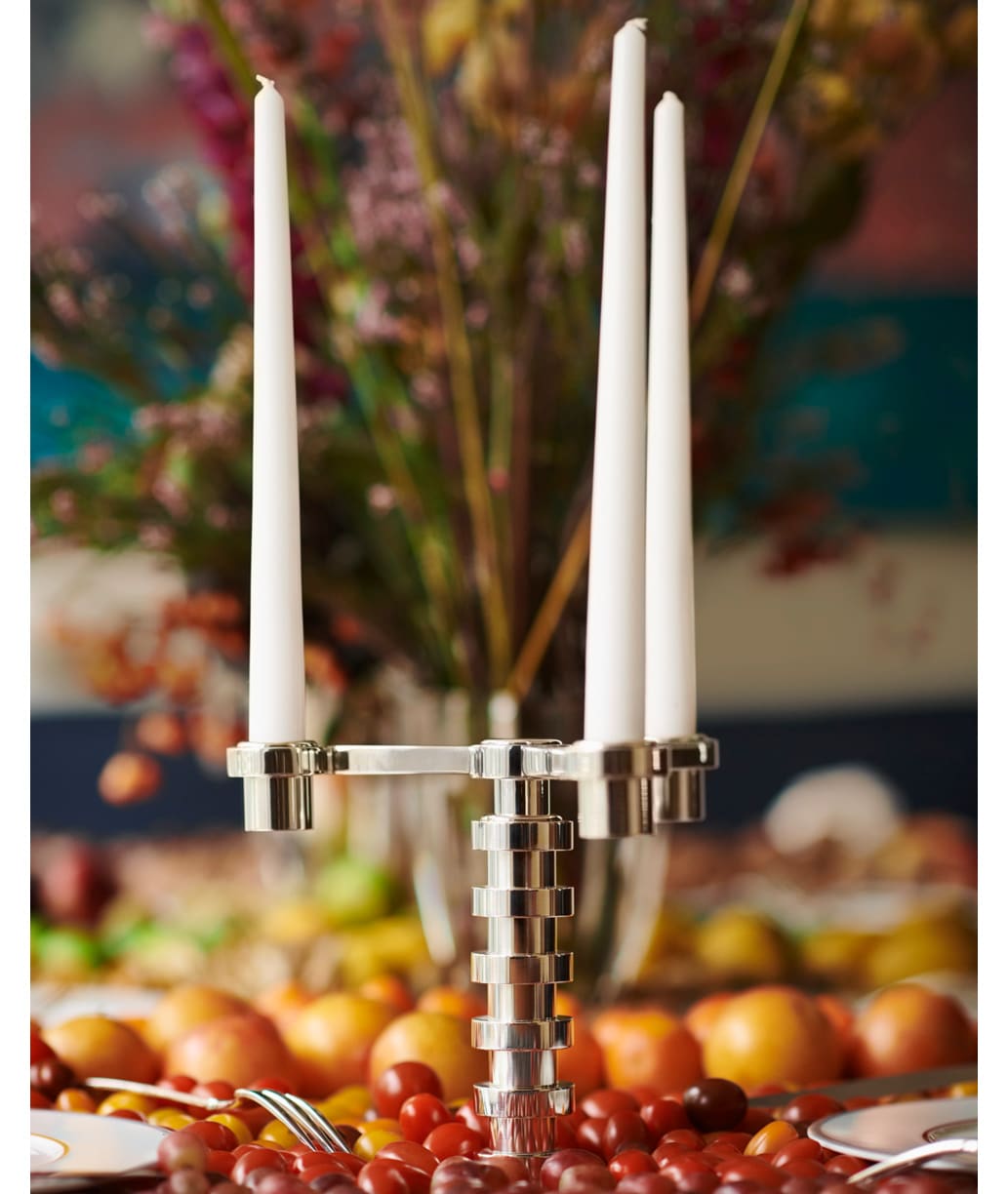 Candélabre 3 lumières en métal argenté de la collection Ruban de Puiforcat, sur une table dressée de fruits et bouquet