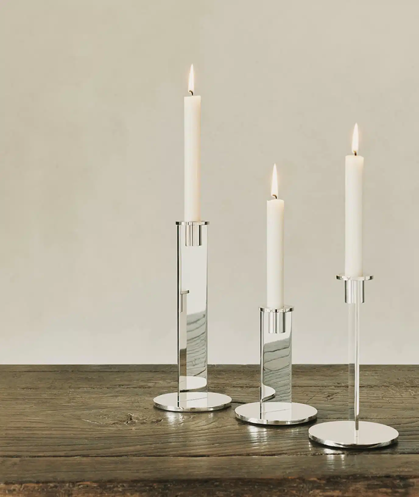 Three candle holders from the Pilotis collection placed on a wooden table