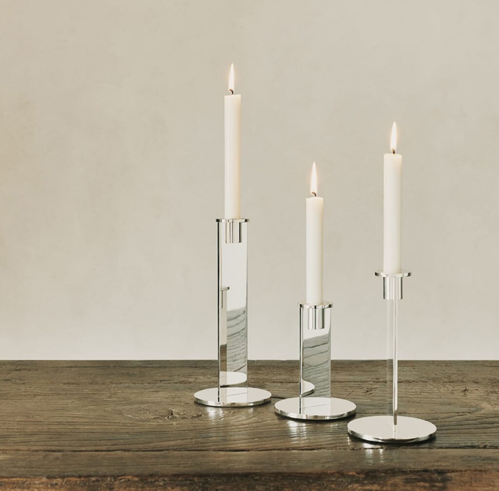 Trois bougeoirs de la collection Pilotis posés sur une table de bois. 