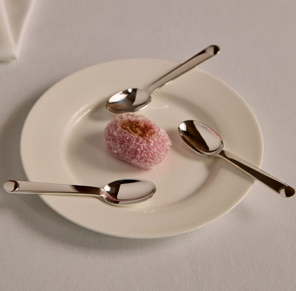 Cuillers de la collection Normandie sur une assiette contenant une pâtisserie asiatique rose sur une nappe blanche