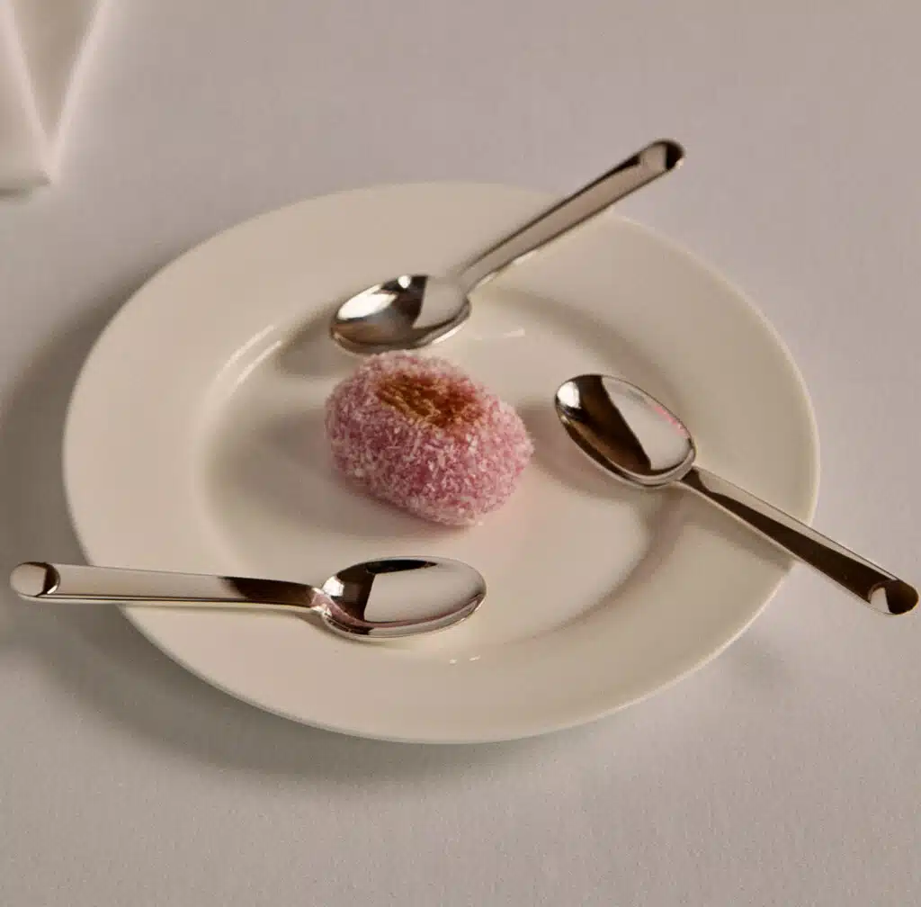 Cuillers de la collection Normandie sur une assiette contenant une pâtisserie asiatique rose sur une nappe blanche